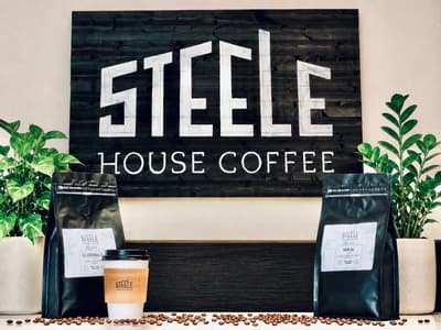 Bagged Steele House Coffee and a to-go cup beside the Steele House Coffee sign